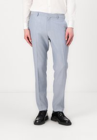 Pantalones azul claro en un corte ajustado, con frente plano, bolsillos laterales y detalle de pliegue; combinados con zapatos negros de cordones.