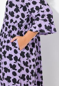Vestido púrpura con estampado floral negro, mangas cortas con volantes, forma acampanada y bolsillos laterales. Fabricado con tejido ligero.