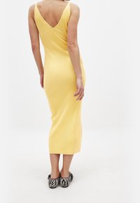 Robe midi jaune à côtes avec un dos en V. La robe a des bretelles fines et une silhouette ajustée. Associée à des chaussures rayées noir et blanc.