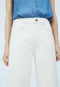 Valkoiset farkut, leveät lahkeet, joissa on viisi taskua, napitus ja korkea vyötärö. Yhdistetty siniseen napilliseen puseroon.