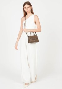 Sac en cuir marron avec une poigne en haut et une sangle amovible, assorti à une combinaison blanche à une épaule et des talons beiges.