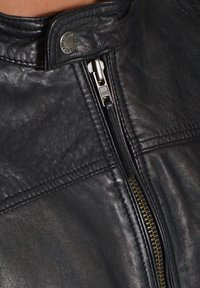 Schwarze Lederjacke mit hohem Kragen, ausgestattet mit einem Metallreißverschluss. Auffälliger YKK-Reißverschlussakzent und strukturiertes Lederfinish.