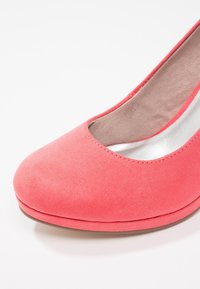 Chaussure plate pour femme en suède rose corail, bout fermé arrondi, doublure intérieure beige rembourrée, sur fond blanc.
