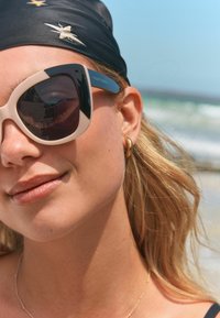 Suurte mustade ja kreemjate raamidega prillid, üliõhulised liblikakujulised ning peegeldavate tumedate läätsedega. Modelil on nähtav kuldne rõngaskõrvarõngas.