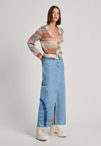 Večbarvna pletena cardigan s V-izrezom, gumbi spredaj, v kombinaciji s svetlo modrim jeans krilom, ki ima sprednji razporek in tie-dye detajl.