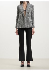 Blazer doppiopetto in tweed bianco e nero con bottoni argentati, abbinato a pantaloni neri a gamba fluida. Texture liscia, design su misura.