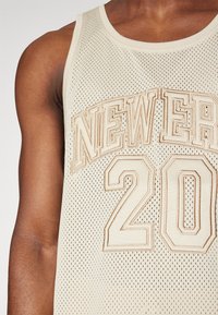 Débardeur en maille beige avec broderie beige "NEWER" et "20", avec un col rond et de larges emmanchures pour la respirabilité.