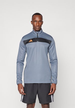 Sudadera atlética gris con cuello alto, cierre de media cremallera y panel en el pecho negro con tres rayas naranjas. Hecha de tejido suave.