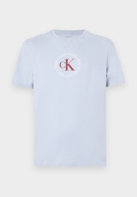 Jasnoniebieska bawełniana koszulka z okrągłym dekoltem, z okrągłym logo w czerwono-białym kolorze z napisem "Calvin Klein New York od 1968 roku".