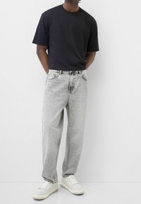 Svart t-shirt, avslappnad passform; ljusgrå, baggy jeans; vita sneakers med grå detaljer; slät textur, inga synliga mönster eller logotyper.