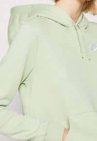 Mintgrön hoodie med en frontficka, dragsko i huvan och en liten vit logotyp på bröstet. Mjuk tyg, avslappnad passform.