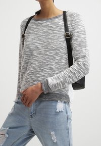 Grauer und weißer, strukturierter Strickpullover mit Rundhalsausschnitt, langen Ärmeln und lockerem Schnitt, kombiniert mit ausgebleichten hellblauen Jeans.