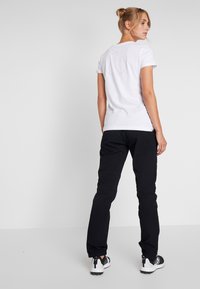T-shirt bianco in cotone con maniche arrotolate, con un design circolare sul retro. Abbinato a pantaloni neri a sigaretta e scarpe da ginnastica nere.