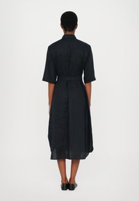 Svart linkjole med kort erm, belted liv og avslappet passform. Har bakgrop og sidespalter for bedre bevegelsesfrihet.