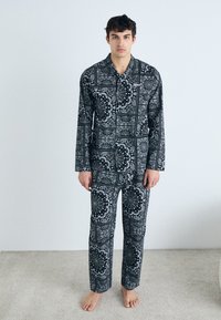 Mustvalge mustriga pidžaama komplekt, mis koosneb pikakä sleeves topist ja sobivatest pükstest, millel on keerukad mustrid ja pehme tekstuur.