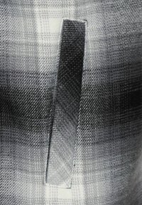 Grå rutigt tyg har en vertikal ficka med en rektangulär öppning, kantad med en subtil söm. Texturen är mjuk och vävd.