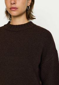 Brun stickad tröja med ribbat mönster, rund halsringning och sänkta axlar. Har ett mjukt, varmt tyg och en avslappnad passform.