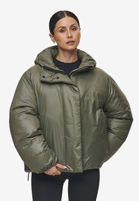 Olijfgroene pufferjas met een capuchon, voorzien van een ritsluiting, gewatteerde textuur en een oversized pasvorm. Middenlang met aanpassingsmogelijkheden.
