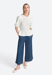 Bílý texturovaný peplum top s krátkými nabíranými rukávy, zkombinovaný s širokými džínovými kalhotami v modré barvě a béžovými plochými botami.
