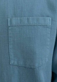 Camicia azzurro chiaro in tessuto testurizzato con una tasca quadrata sul petto. Il tessuto presenta un leggero motivo intrecciato ed è caratterizzato da una vestibilità comoda.