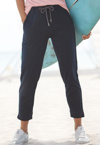 Marineblaue Jogginghose mit lockerer Passform, schmal zulaufenden Knöcheln, aus einem weichen Material. Kombiniert mit weißen Sneakers und einem hellrosa Oberteil.