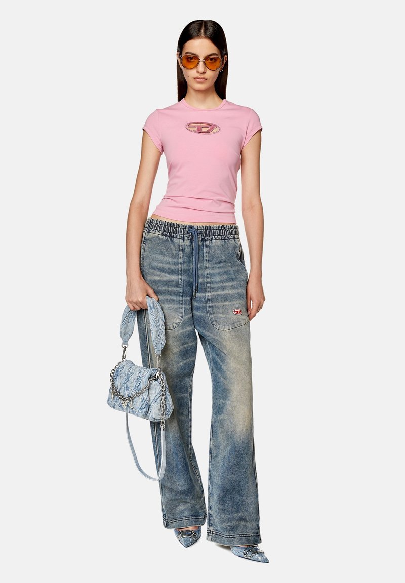 Roze fitted t-shirt met logo, lichtblauwe denim wijd uitlopende broek, blauwe handtas met patroon en blauwe pumps met spitse neus. Oranje zonnebril.