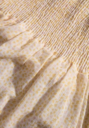 Smocked dress fabric features a white background with yellow and pink floral patterns. Textured, lightweight material with soft gathers.