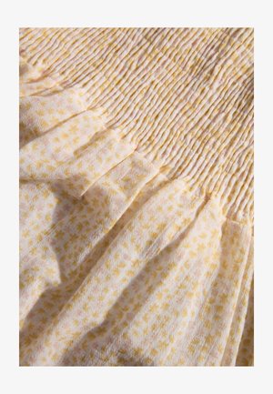 Der Stoff des gesmokten Kleides hat einen weißen Hintergrund mit gelben und rosa Blumenmustern. Das strukturierte, leichte Material verfügt über sanfte Raffungen.