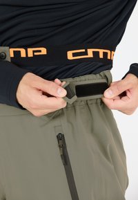 Grüne Skihosen mit einem schwarzen Bund, orangefarbenem "CMP"-Logo, verstellbarem Klettverschluss und Reißverschlusstasche.