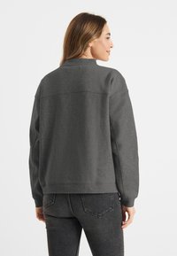 Grijze sweatshirt met een oversized pasvorm, geribde manchetten en een textuurstof. De achterkant heeft een horizontale naaddetails. Gecombineerd met donkere jeans.