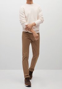 Jasnobeżowy sweter z prążkowanymi mankietami, zestawiony z brązowymi spodniami o wąskim kroju i brązowymi trampkami. Gładka tekstura i casualowy design.