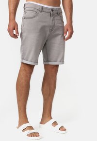 Shorts en denim gris avec des ourlets roulés, dotés de poches avant et d'une fermeture à bouton. Portés avec des sandales blanches, mettant en avant un design décontracté.
