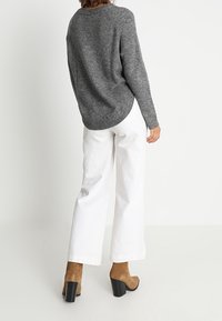 Maglione grigio a maglia con maniche lunghe, abbinato a pantaloni bianchi a gamba larga e stivaletti con tacco a blocco color cammello. Tessuto morbido, vestibilità comoda.
