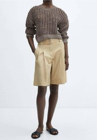 Pull marron en maille ajourée, short plissé beige et sandales slides noires. Design simple et palette de couleurs neutres.