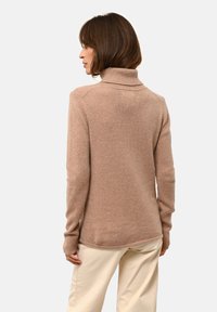 Pull-over en col roulé couleur marron clair, fabriqué à partir d'un tissu doux et confortable. Il présente un col et des poignets côtelés, avec un ourlet arrière légèrement plus long.