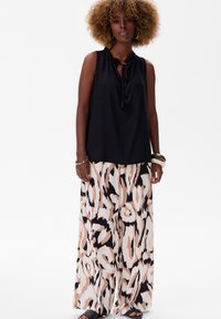 Czarny top bez rękawów z detalem nawiązującym do wiązania, zestawiony z szerokimi spodniami w różowy, beżowy i czarny abstrakcyjny wzór. Gładka tekstura materiału.