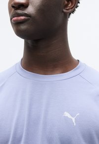 Ανοιχτό μωβ κοντομάνικη μπλούζα με στρογγυλή λαιμόκοψη και λευκό λογότυπο Puma στο στήθος. Ομαλή, απαλή υφή υφάσματος.