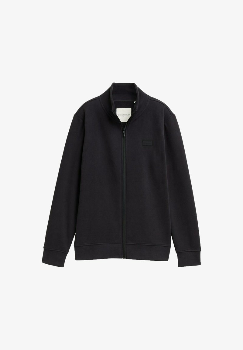 Giacca nera con zip e colletto alto, realizzata in un tessuto morbido. Presenta un design minimalista e una piccola toppa con logo sul lato sinistro del petto.
