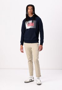 Felpa blu navy con stampa grafica bianca e rossa, dotata di tasca a canguro. Abbinate a pantaloni slim-fit beige chiaro e sneakers casual.