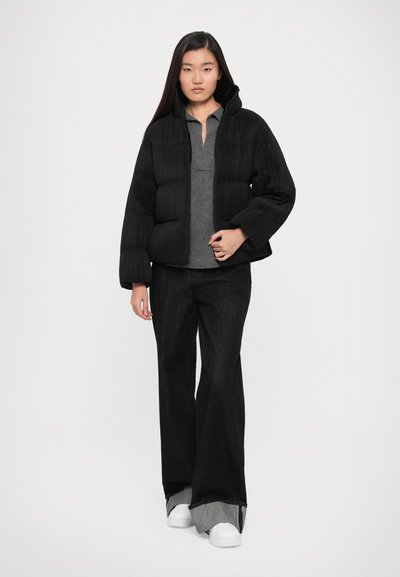 Black puffer jacket with a textured finish, high collar, and fitted cuffs, paired with dark jeans and white sneakers.