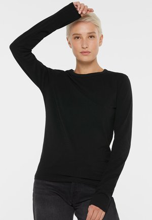 Black long-sleeve top made of soft fabric. Features a round neckline and fitted sleeves. Worn with dark jeans against a plain white background.