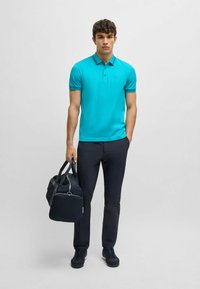 Turkos polo-tröja med korta ärmar, stängning med övre knapp, tillsammans med navybyxor och en matchande duffelväska. Också avslappnade skor ingår.