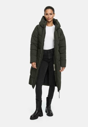 Long, padded olive green coat with a hood, quilted design, and front zipper. Worn over a white shirt and paired with black jeans and boots.