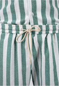 Pantalon rayé verticalement vert et blanc avec une taille élastique et un cordon beige noué en nœud devant.