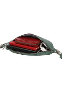 Petite pochette verte zippée contenant un portefeuille rouge, deux carnets et des écouteurs blancs à l'intérieur.