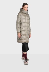 Ljusbrun vadderad jacka med hög krage, diagonalt quiltat mönster och sidofickor med blixtlås. Matchad med en svart kjol och rosa sneakers.