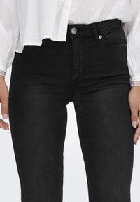 Svart høy midje jeans laget av denim, med en jevn tekstur, klassisk fem-lommers design og en frontåpning med knapp.