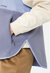 Hellblau und weich graue Fleece-Weste mit einem weißen Innenfutter, ausgestattet mit einer Seitentasche und kontrastierenden Abschlüssen entlang dem Saum.
