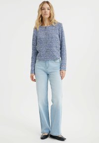 Giacca lavorata a maglia blu con colletto rotondo, chiusura a bottoni e maniche lunghe, abbinata a jeans svasati azzurri e ballerine nere.