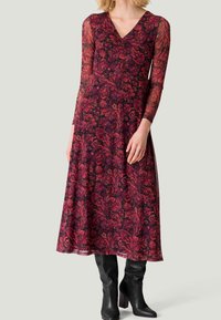 Långärmad klänning i djup bourgogne och rosa med blommönster, featuring V-ringning och genomskinliga ärmar. Kombinerad med åtsittande svarta knähöga stövlar.